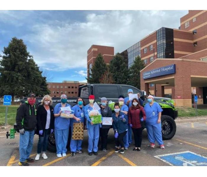 group of people some nurses some not, standing in front of a black truck holding baskets of goodies brought to them