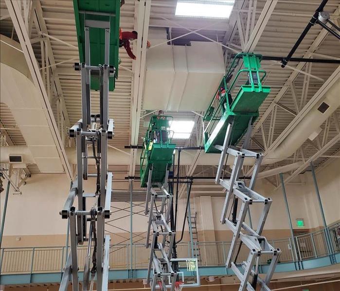 Electric lifts raising fire restoration techs up to a tall ceiling to remove smoke and soot damage